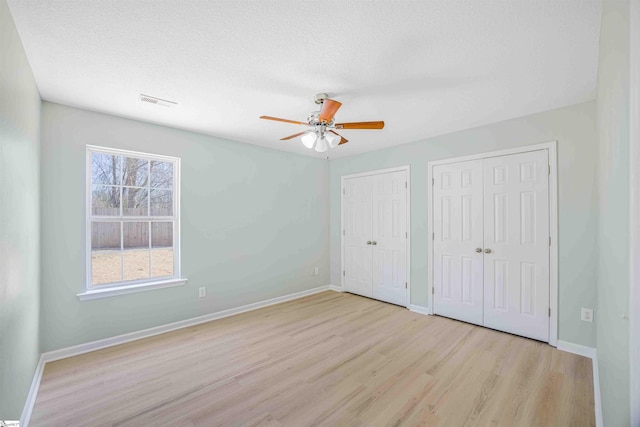 unfurnished bedroom with baseboards, light wood-style flooring, ceiling fan, a textured ceiling, and two closets