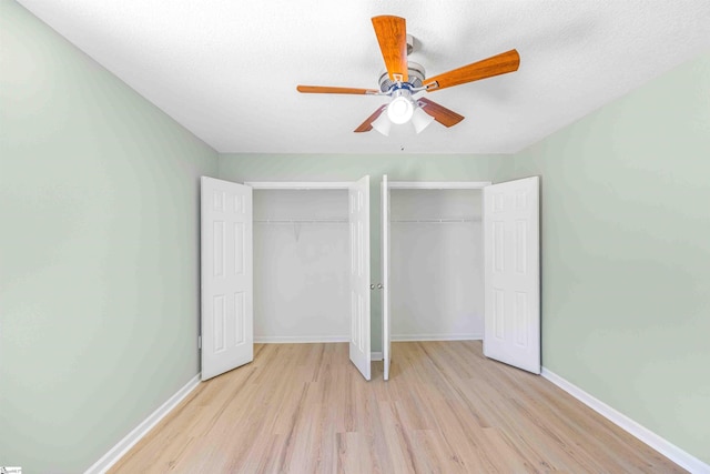 unfurnished bedroom featuring a textured ceiling, a ceiling fan, baseboards, light wood-style floors, and two closets