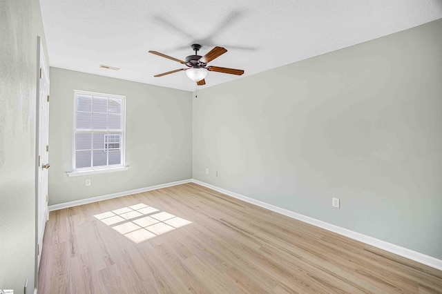 spare room featuring baseboards, visible vents, ceiling fan, and wood finished floors