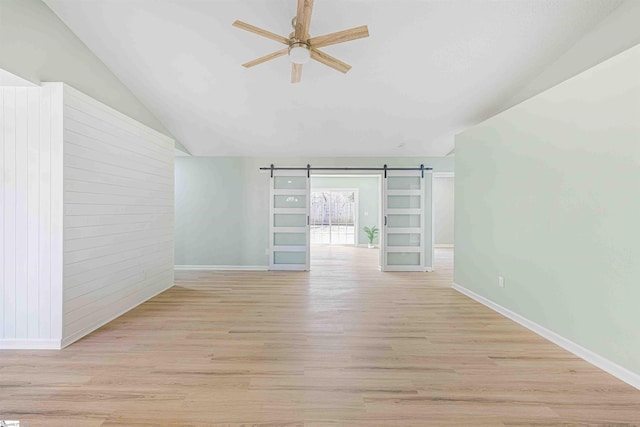 unfurnished room with a barn door, baseboards, ceiling fan, light wood-style flooring, and vaulted ceiling