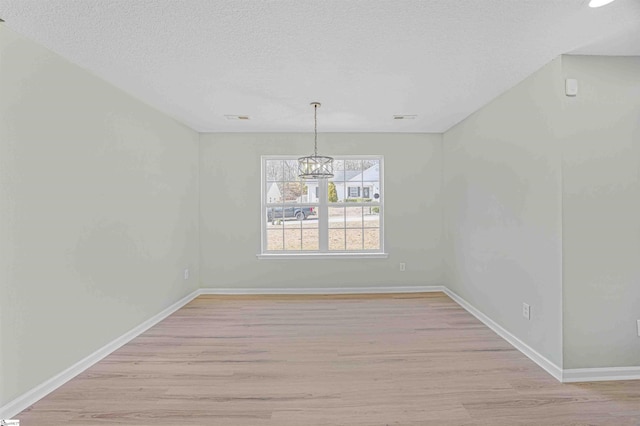 unfurnished dining area featuring a textured ceiling, light wood finished floors, an inviting chandelier, and baseboards