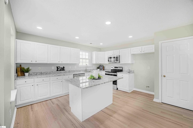 kitchen with light wood finished floors, appliances with stainless steel finishes, white cabinetry, a sink, and light stone countertops