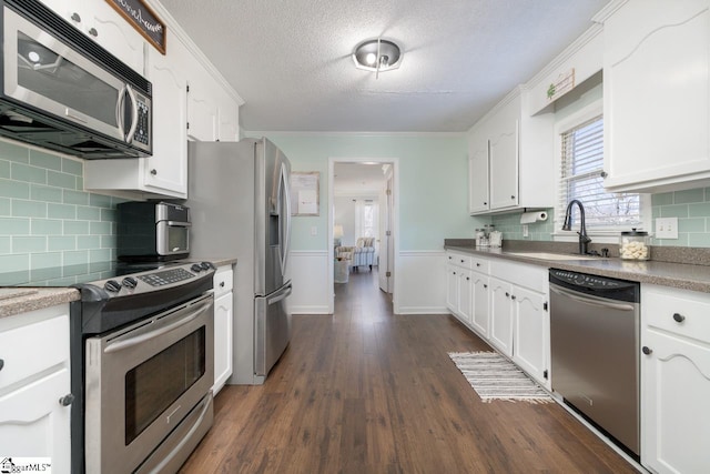 kitchen with dark wood-type flooring, a sink, white cabinets, appliances with stainless steel finishes, and crown molding