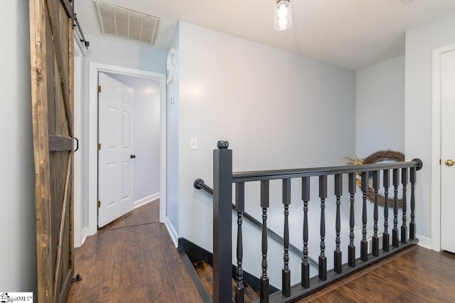 hall with a barn door, baseboards, visible vents, wood finished floors, and an upstairs landing