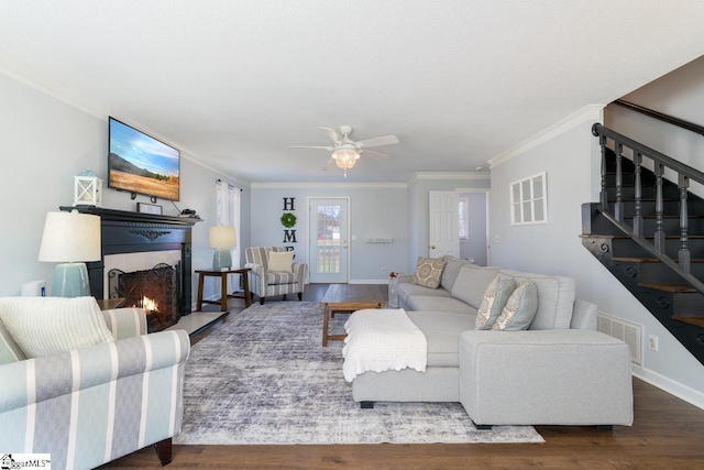 living area featuring visible vents, stairway, wood finished floors, a lit fireplace, and crown molding