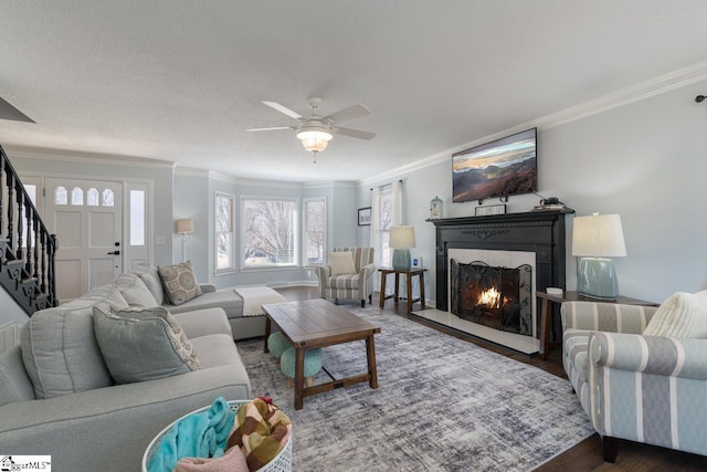 living area featuring crown molding, stairway, a ceiling fan, wood finished floors, and a warm lit fireplace