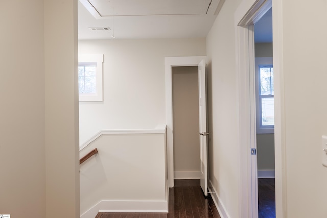 corridor with dark wood-style flooring, visible vents, attic access, an upstairs landing, and baseboards