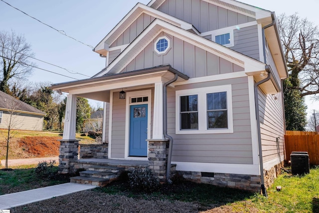 craftsman-style home with covered porch, cooling unit, board and batten siding, and fence