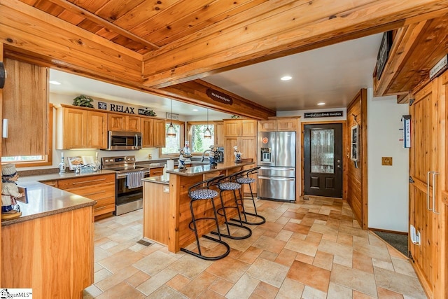 kitchen with pendant lighting, appliances with stainless steel finishes, stone finish floor, beamed ceiling, and a kitchen breakfast bar