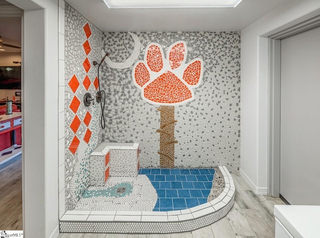 full bath featuring wood finished floors, a tile shower, and baseboards