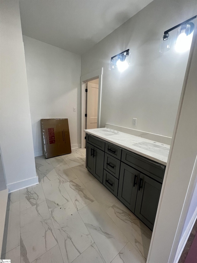 bathroom with marble finish floor, double vanity, a sink, and baseboards