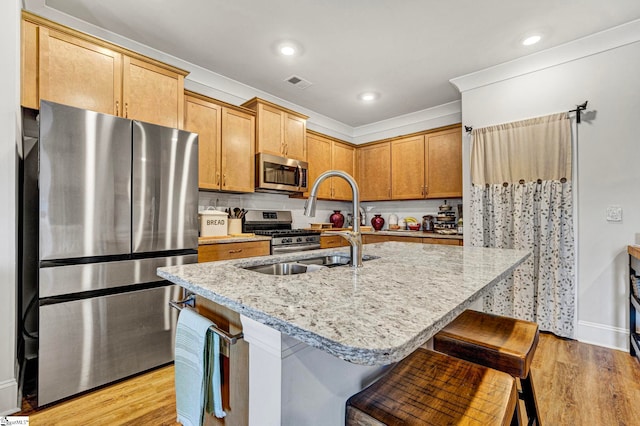 kitchen with light wood finished floors, a center island with sink, visible vents, appliances with stainless steel finishes, and light stone countertops