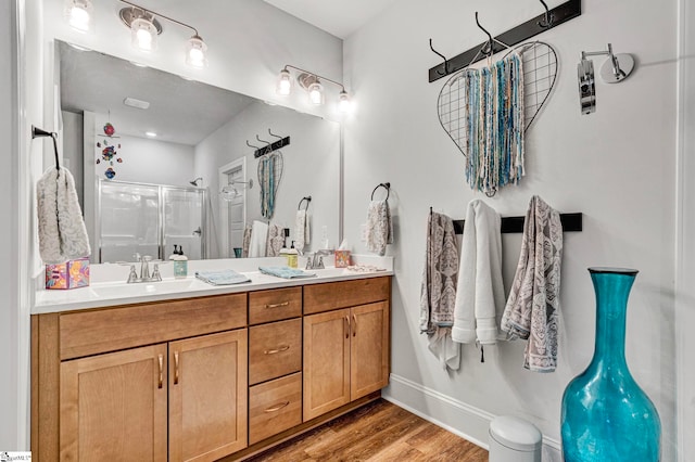 full bath with a stall shower, double vanity, a sink, and wood finished floors