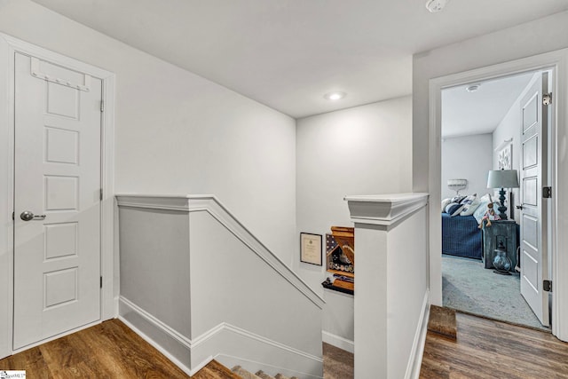 hallway featuring baseboards, wood finished floors, and an upstairs landing