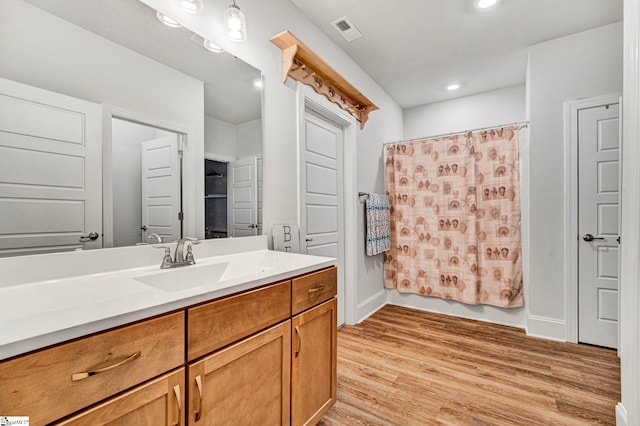 bathroom featuring baseboards, visible vents, wood finished floors, vanity, and recessed lighting