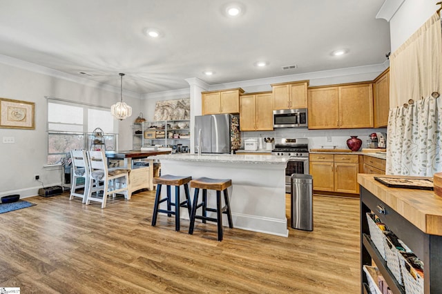 kitchen with stainless steel appliances, ornamental molding, light wood-type flooring, and a center island