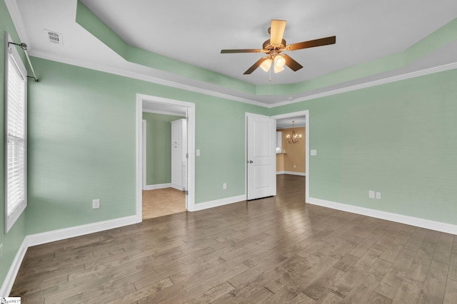 unfurnished bedroom featuring a tray ceiling, multiple windows, wood finished floors, and visible vents