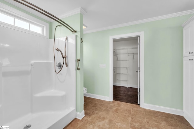 bathroom with baseboards, toilet, a spacious closet, crown molding, and a shower stall