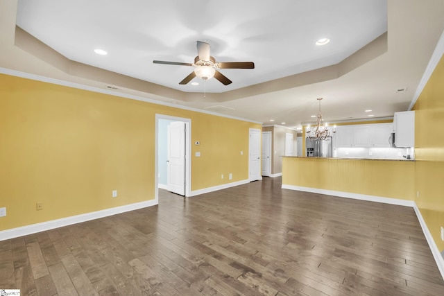 unfurnished living room with a tray ceiling, dark wood-style flooring, ornamental molding, baseboards, and ceiling fan with notable chandelier