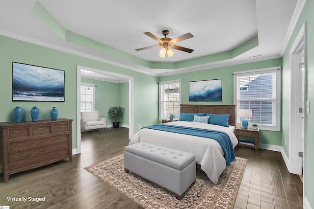 bedroom featuring baseboards, multiple windows, a tray ceiling, and wood finished floors