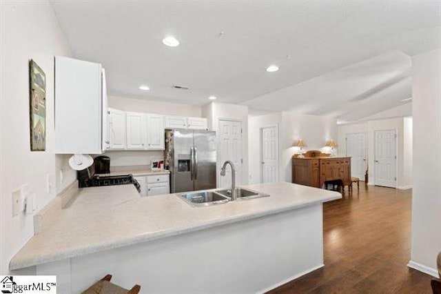 kitchen featuring a peninsula, stove, a sink, light countertops, and stainless steel fridge