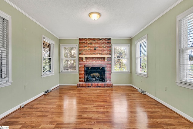 unfurnished living room featuring a brick fireplace, visible vents, wood finished floors, and ornamental molding