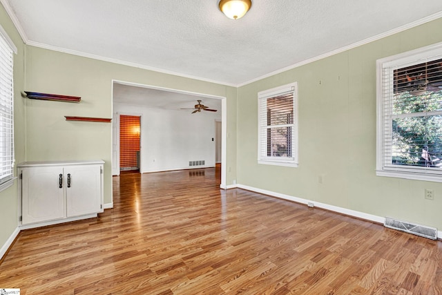 spare room with light wood-type flooring, visible vents, a ceiling fan, and ornamental molding