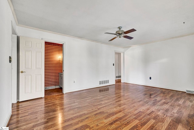 empty room featuring ornamental molding, visible vents, baseboards, and wood finished floors