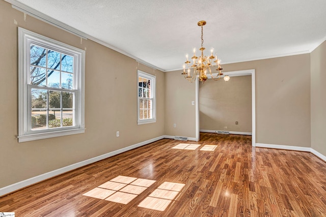 interior space featuring ornamental molding, a textured ceiling, wood finished floors, a chandelier, and baseboards