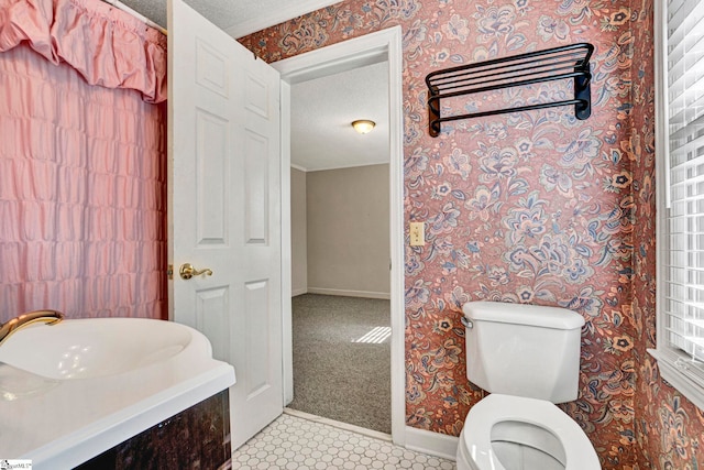 half bath featuring toilet, a sink, a textured ceiling, baseboards, and wallpapered walls