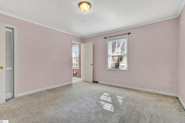 carpeted spare room with ornamental molding, a textured ceiling, and baseboards