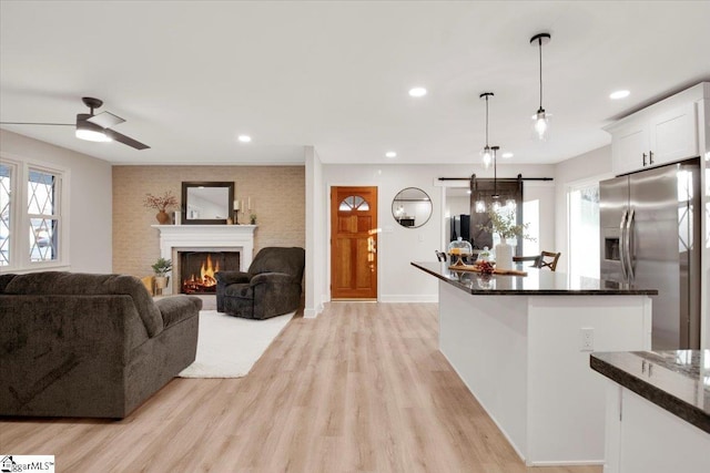 kitchen featuring a barn door, a lit fireplace, stainless steel refrigerator with ice dispenser, and light wood-style flooring