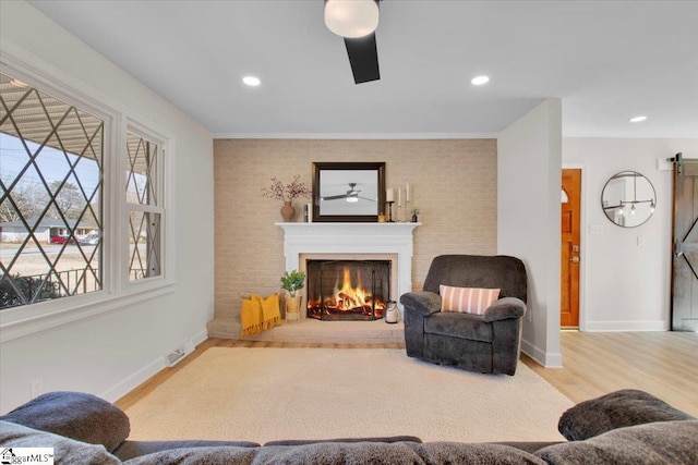 living area featuring a barn door, ceiling fan, wood finished floors, a warm lit fireplace, and baseboards