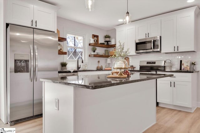 kitchen featuring open shelves, tasteful backsplash, appliances with stainless steel finishes, light wood-style floors, and dark stone countertops