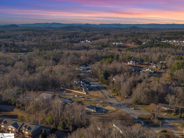 aerial view at dusk featuring a mountain view and a view of trees