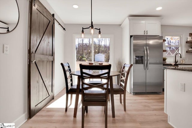 dining space with recessed lighting, a healthy amount of sunlight, light wood-style flooring, and a barn door