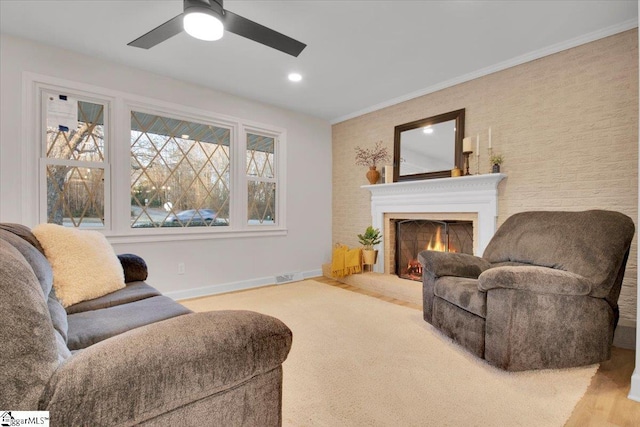 carpeted living area with a warm lit fireplace, ceiling fan, crown molding, and baseboards