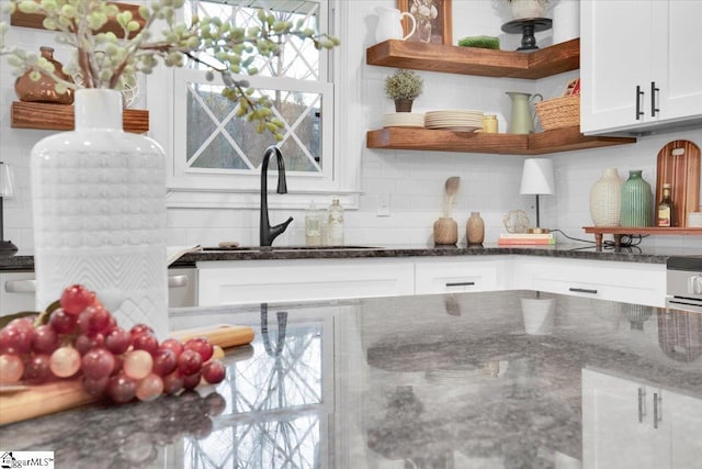 kitchen featuring white cabinets, dark stone countertops, a sink, open shelves, and backsplash