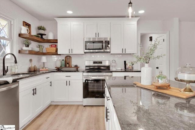 kitchen with light wood finished floors, decorative backsplash, appliances with stainless steel finishes, white cabinetry, and a sink