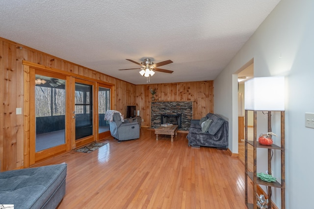 living area with a textured ceiling, ceiling fan, light wood-style flooring, wood walls, and a fireplace