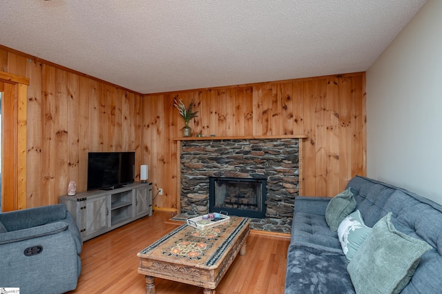 living room featuring a textured ceiling, wooden walls, wood finished floors, and a stone fireplace