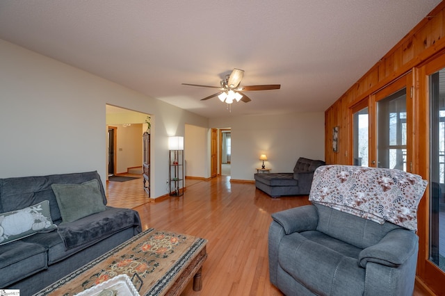 living area featuring light wood-style floors, a ceiling fan, wood walls, a textured ceiling, and baseboards