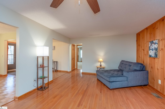 living area with a ceiling fan, visible vents, wood walls, and light wood-style flooring