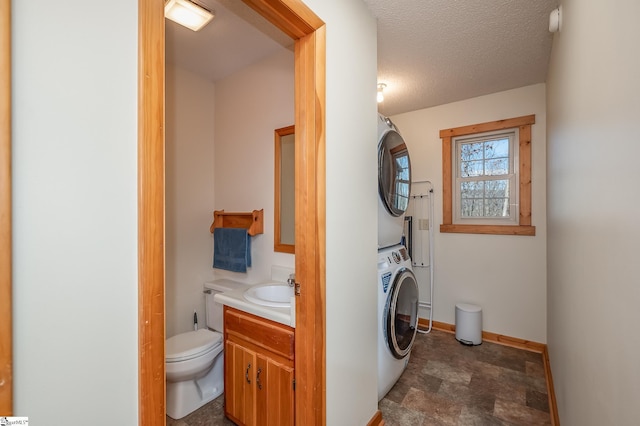 washroom featuring stacked washer and dryer, a sink, a textured ceiling, laundry area, and baseboards