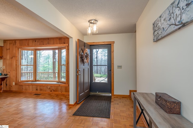 entryway with plenty of natural light, wooden walls, baseboards, and a textured ceiling