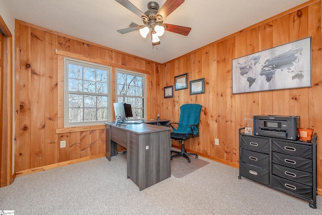 home office with a textured ceiling, wooden walls, ceiling fan, and light colored carpet