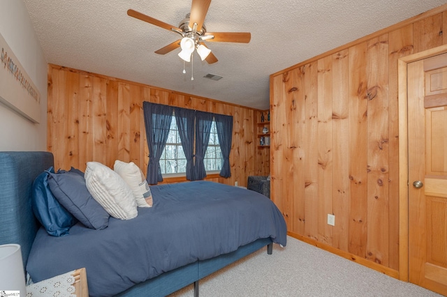 carpeted bedroom with wood walls, a ceiling fan, visible vents, and a textured ceiling