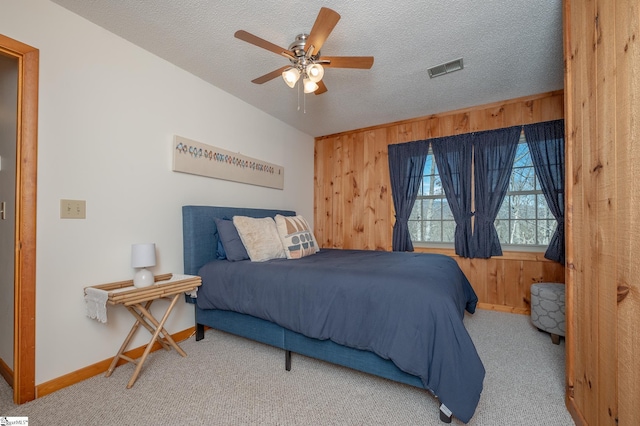 bedroom featuring carpet, wooden walls, visible vents, and a textured ceiling