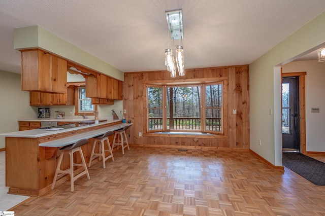 kitchen with light countertops, brown cabinetry, wood walls, a textured ceiling, and baseboards