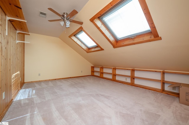 additional living space featuring light carpet, vaulted ceiling with skylight, visible vents, baseboards, and ceiling fan